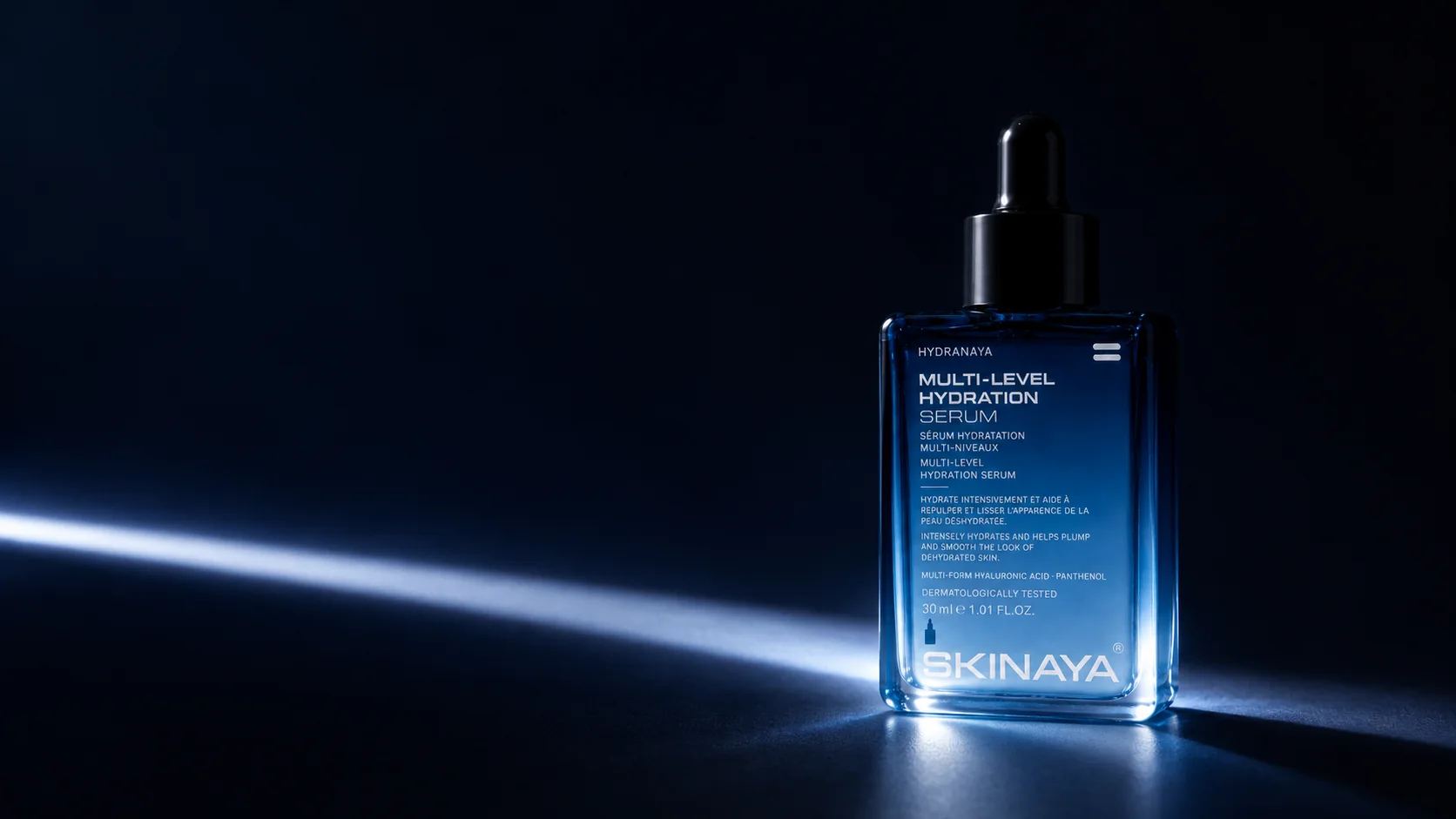 The HYDRANAYA serum in a dark navy studio, revealed by a single blade of light