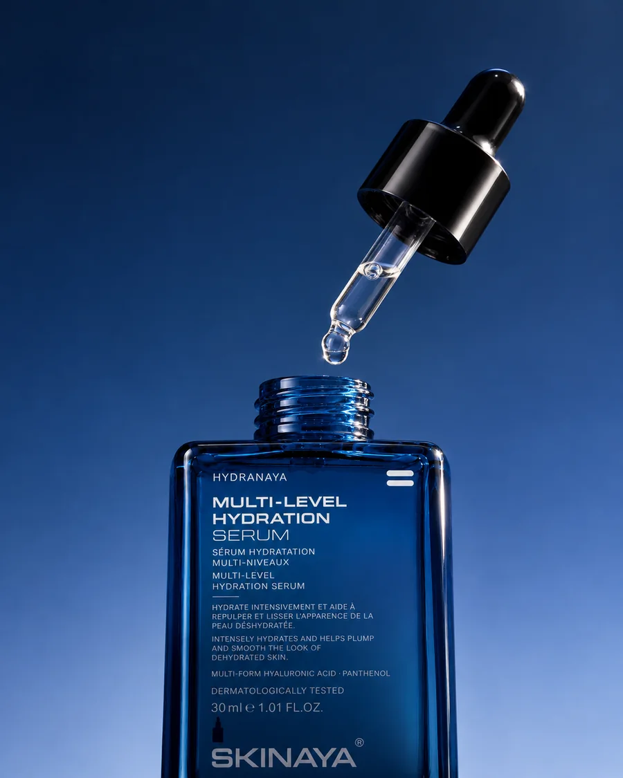 The open HYDRANAYA serum bottle with its dropper floating above it against deep cobalt