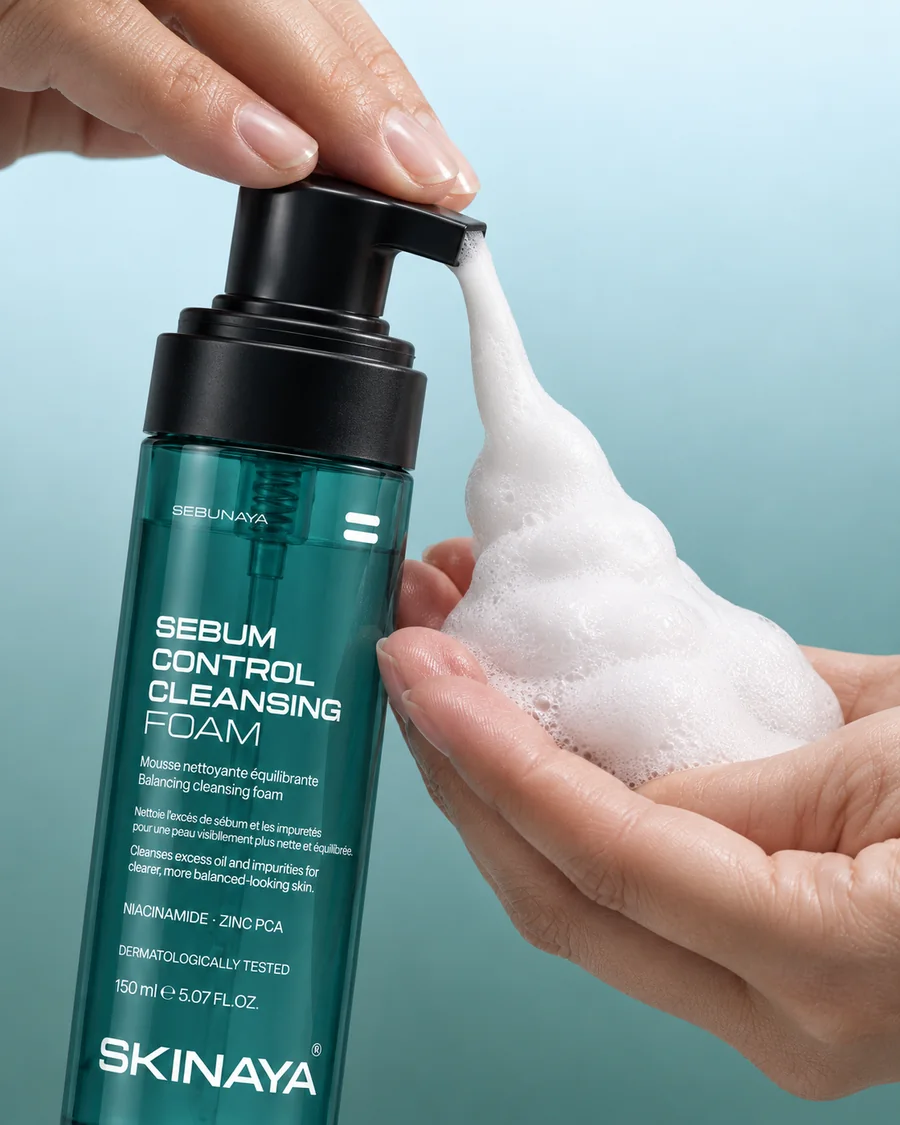 A hand pressing the SEBUNAYA Sebum Control Cleansing Foam pump, white foam rising into the other palm